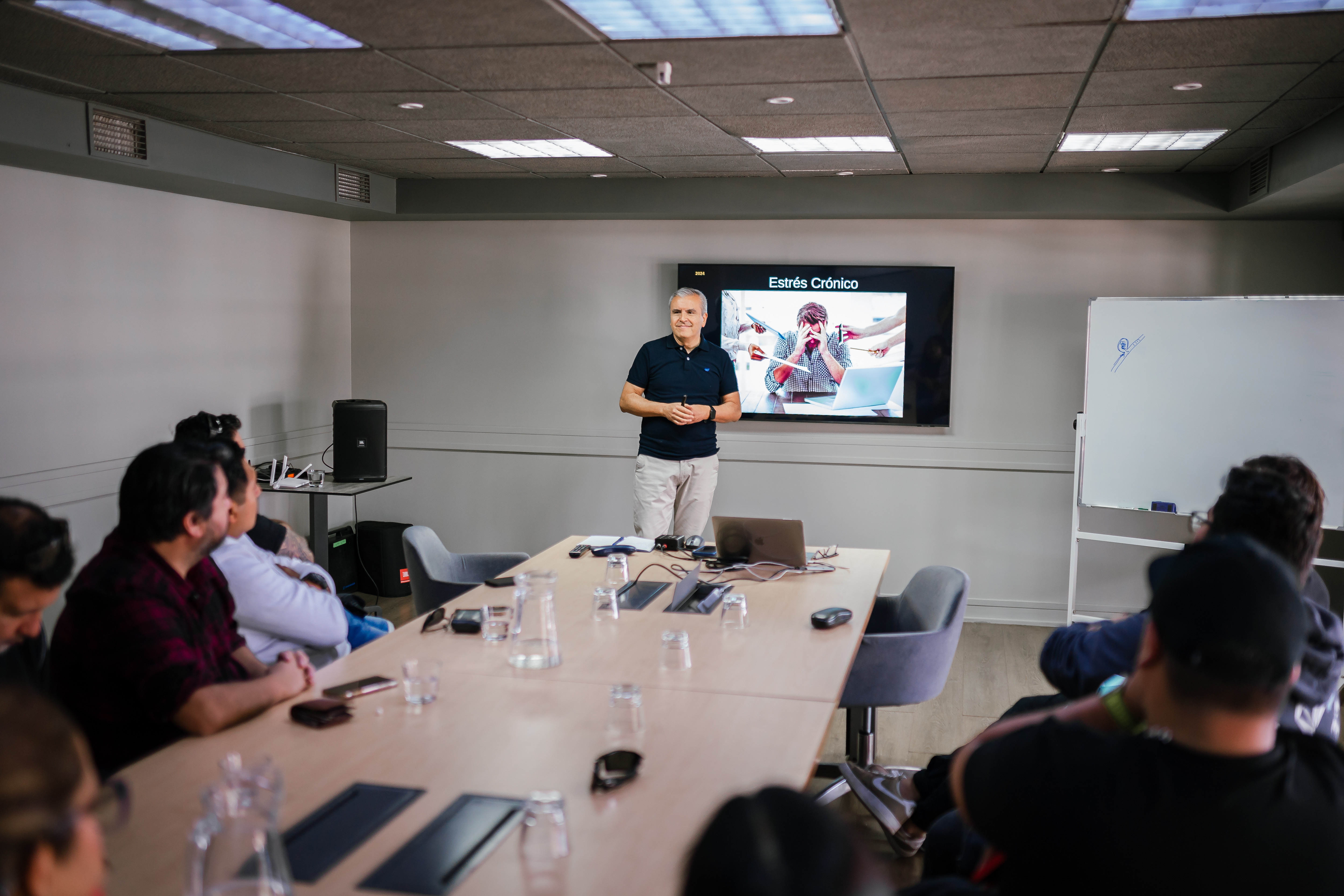 Carlos Martínez facilitando una formación presencial junto a una pizarra y una pantalla de apoyo, guiando un ejercicio práctico de reflexión y desarrollo personal en un contexto de aprendizaje grupal.